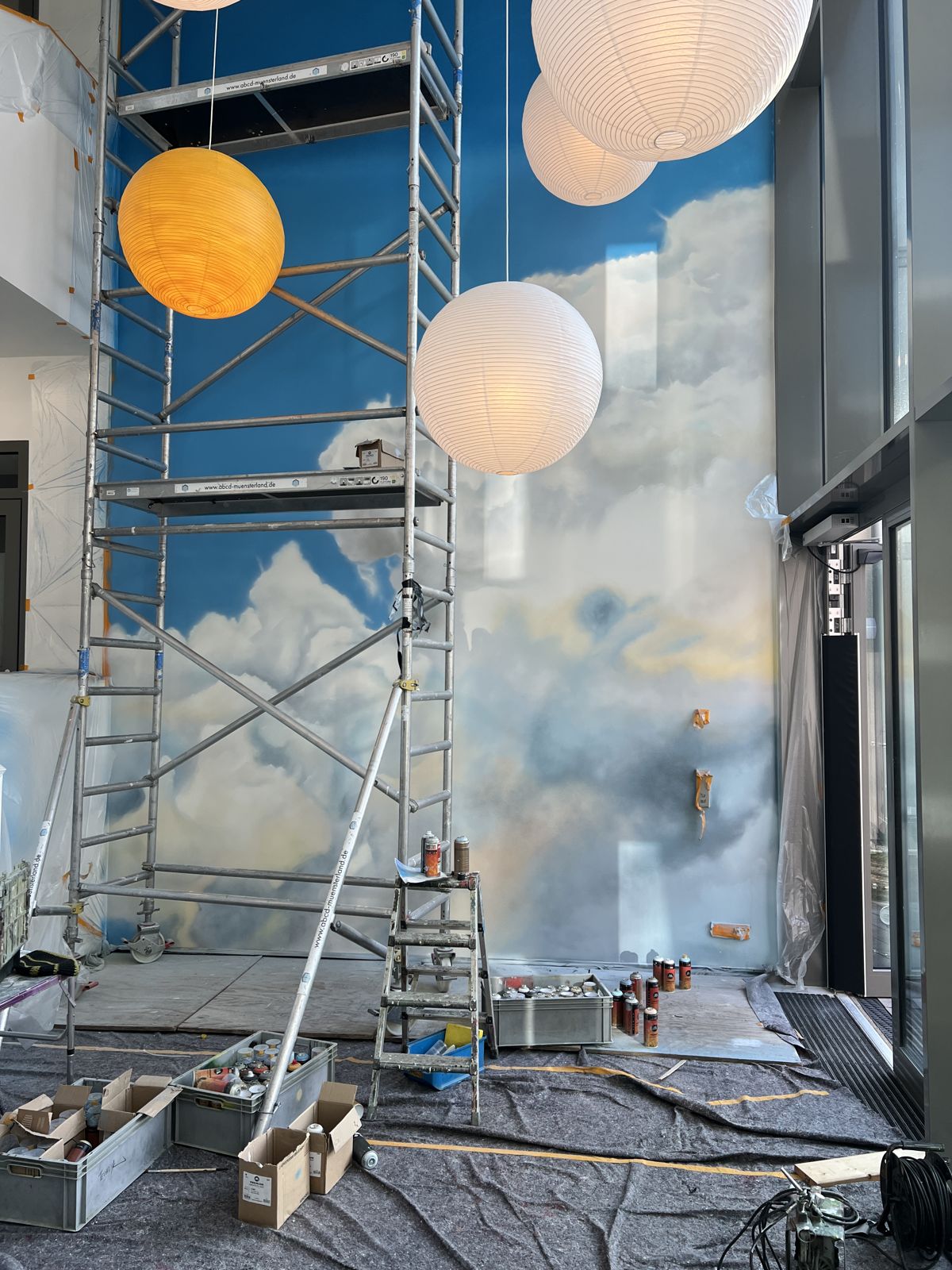 Das Foyer der Arche Tecklenburg während der Gestaltung: Wolkenhimmel an der hohen Wand, Gerüst und Papierlampen