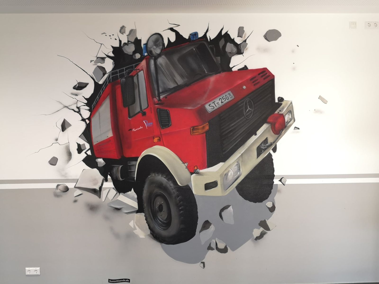 Graffiti-Unimog der Feuerwehr Rheine bricht im Eingangsbereich durch die Wand, 3D-Illusion